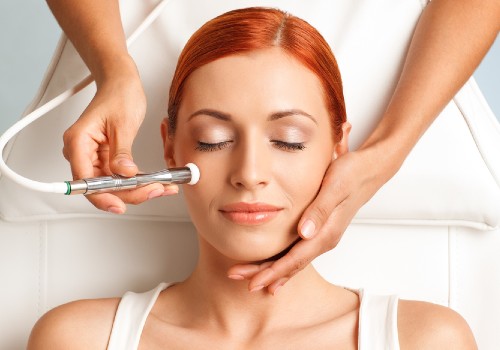 Practitioner moving a metal microdermabrasion wand across a reclining woman's cheek