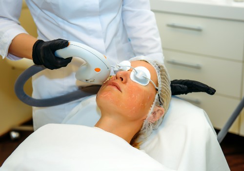 Practitioner using a light-based facial treatment device on a woman wearing protective eye shields