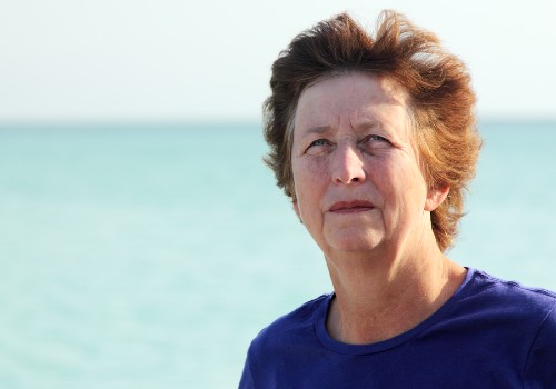 Woman in a blue top standing outdoors beside the sea with sunlight on her face