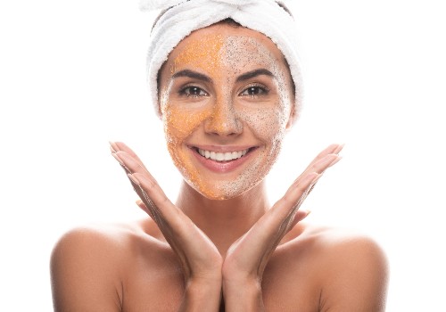 Smiling woman with exfoliating scrub on her face and a towel wrapped around her hair
