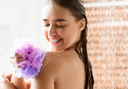 Woman washing her shoulder with a purple mesh shower puff under running water