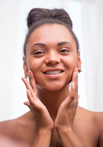 Smiling woman with her hair in a bun gently resting both hands against her cheeks