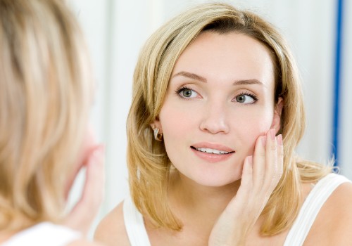 Woman touching her cheek while looking at her reflection in a bathroom mirror