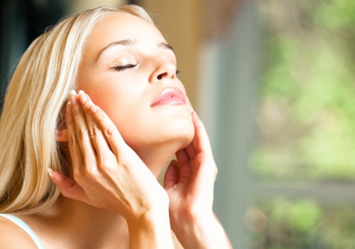 Woman with her eyes closed holding both hands against her jaw beside a sunny window
