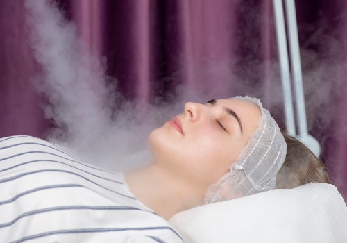 Woman lying on a treatment bed with her eyes closed as steam rises around her face