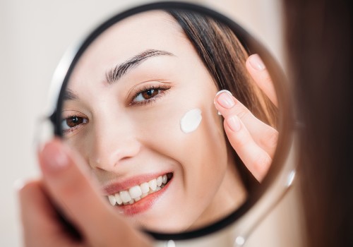 Woman smiling into a round mirror while dabbing a small amount of cream onto her cheek