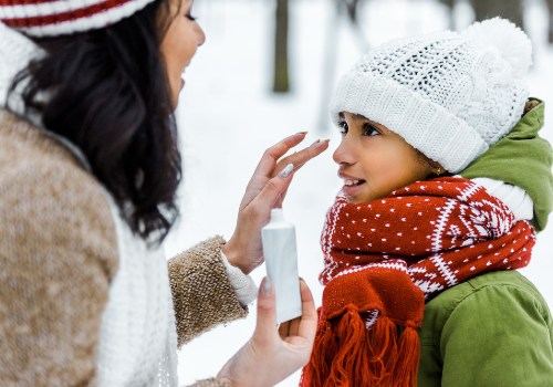 Woman applying cream to a child's face outdoors while the child wears a knitted hat and scarf