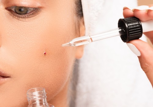 Close-up of a woman holding a glass serum dropper beside a small spot on her cheek