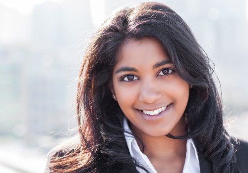Smiling woman with long dark hair posing outdoors against a softly blurred background